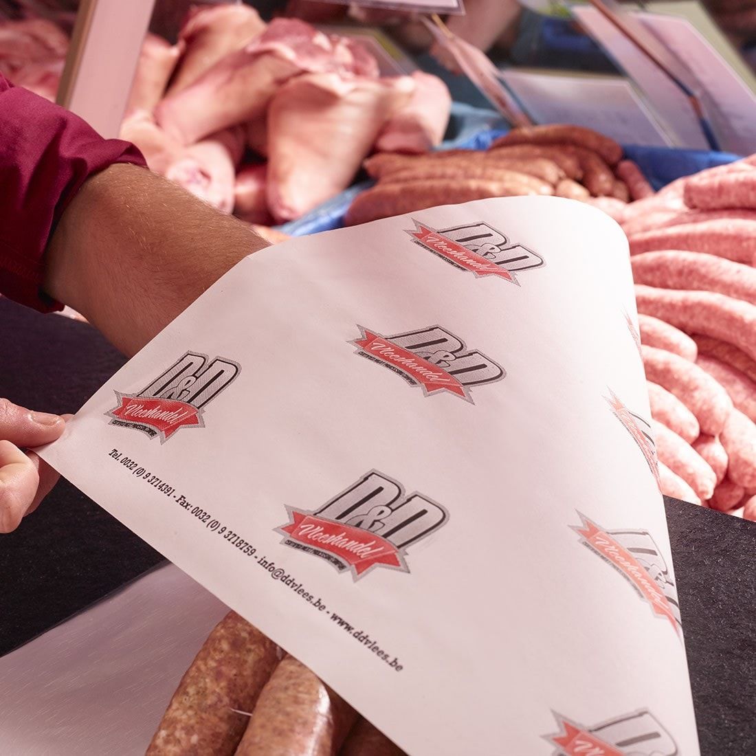 Een hand houdt worsten in wit D&D-papier boven de toonbank